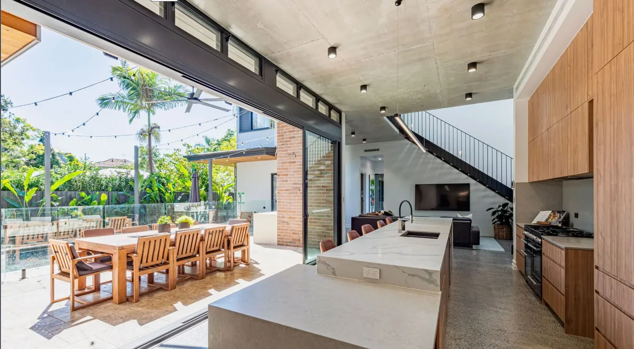 Aluminium bi-fold doors and highlight windows opening a kitchen onto a pool terrace
