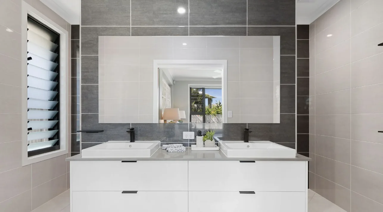 Large frameless vanity mirror above a double basin in a tiled bathroom